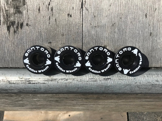 Four black Santoro Fabworx Cadillac crash bar wheels with white lettering lined up on wood